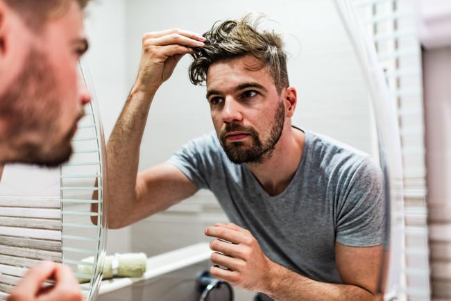 man looking in mirror for hair loss